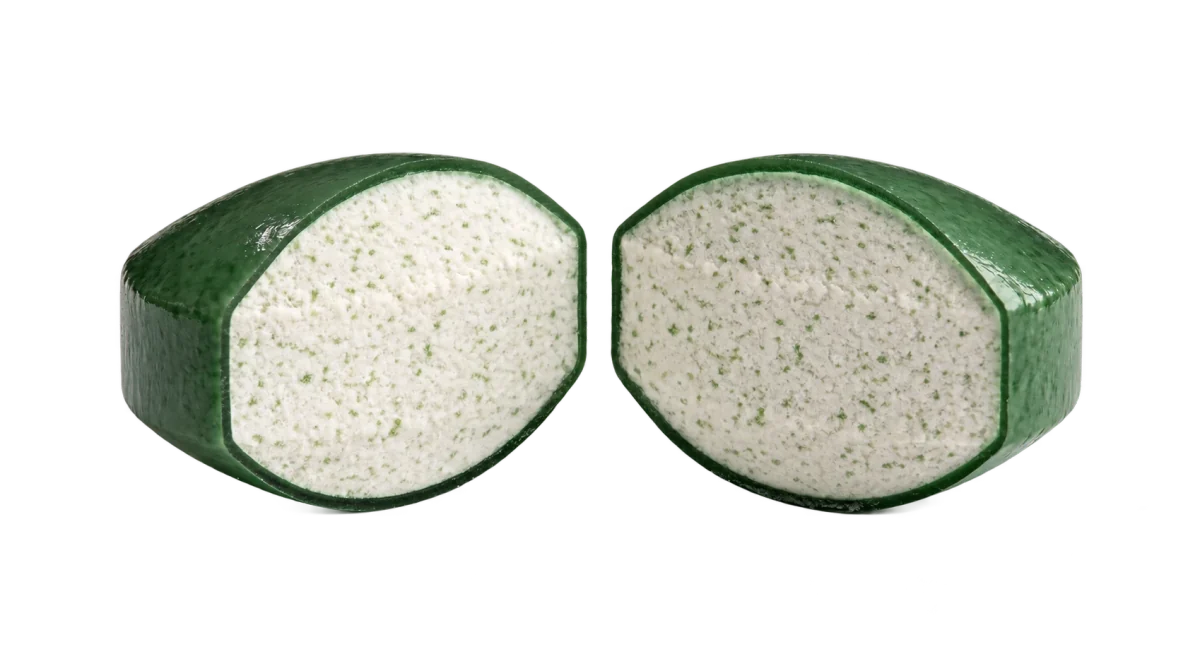 A coated tablet cut in half to reveal its nutrient core and thin green polymer coating.